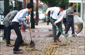 Des employés de bureau balayant des feuilles sur le trottoir de l'entreprise. 